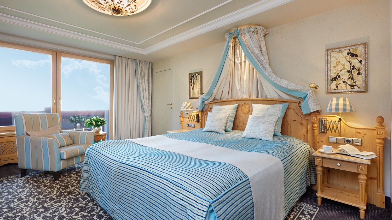 Doppelzimmer Deluxe Elegantes Hotelzimmer mit großem Bett, stilvollen Möbeln und Blick durch große Fenster.
