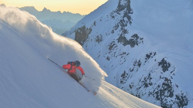 Skifahrer fährt eine verschneite Piste mit Bergen im Hintergrund hinunter, ideal für Wintersportler.