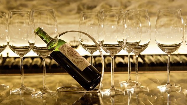A bottle of wine surrounded by fine wine glasses on a wooden table in the wine cellar.