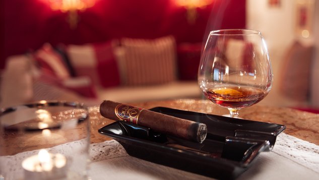An ashtray with a cigar inside and an alcoholic drink on the side
