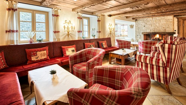 Stube mit roten Sesseln, Sofas und alpiner Einrichtung.