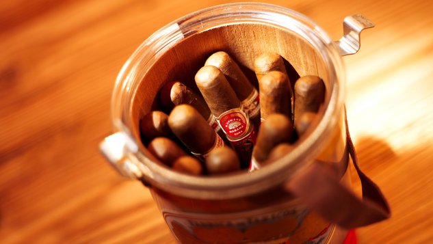A glass full of fine cigars arranged on a warm wooden table.