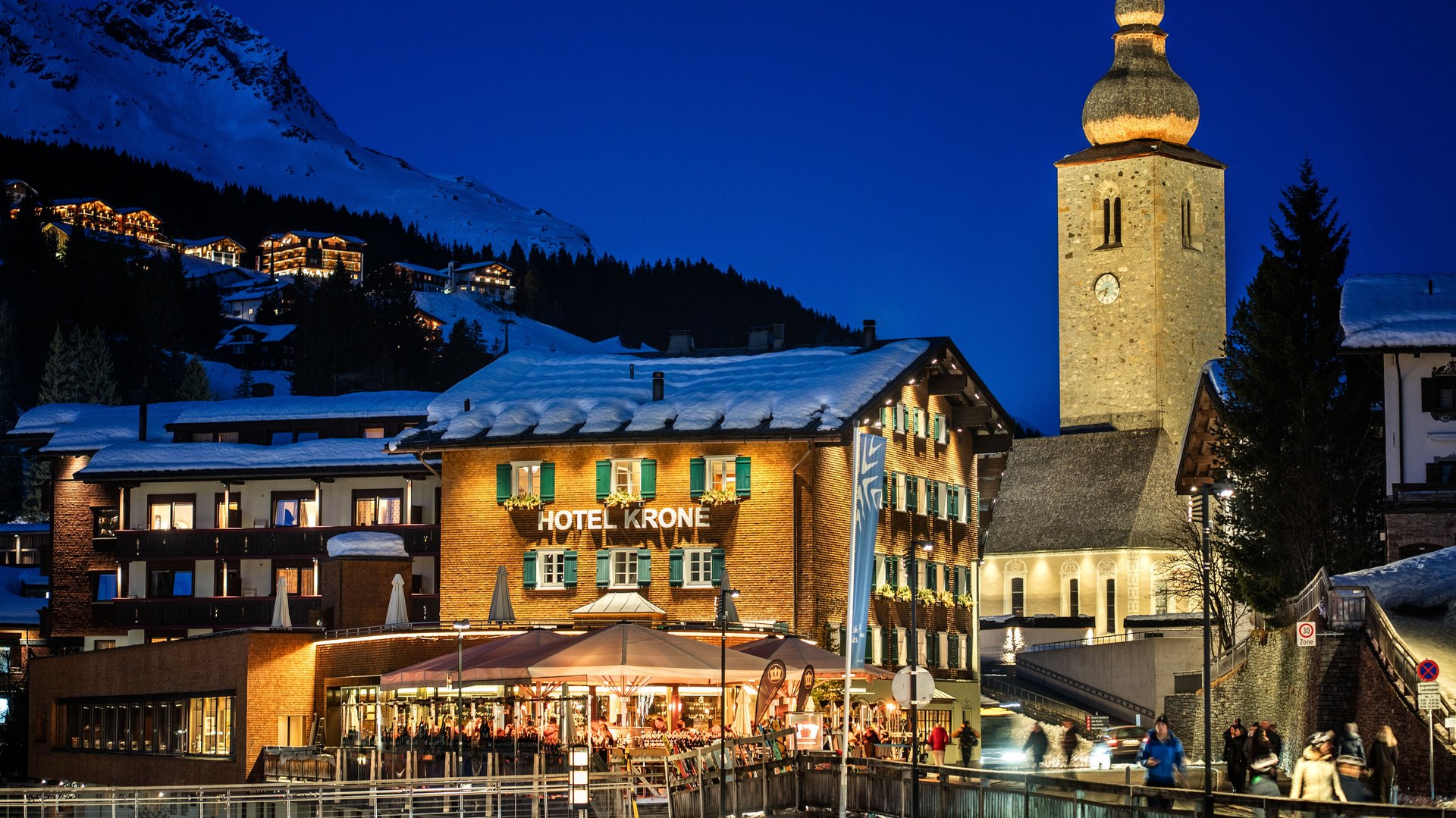 Hotel und Kirchturm in einem Bergdorf bei Nacht mit beleuchtetem Himmel im Hintergrund