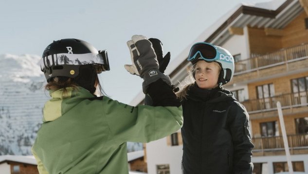 Zwei Personen, ein Kind und ein Erwachsener, machen einen High-Five im Schnee mit Wintersportkleidung.