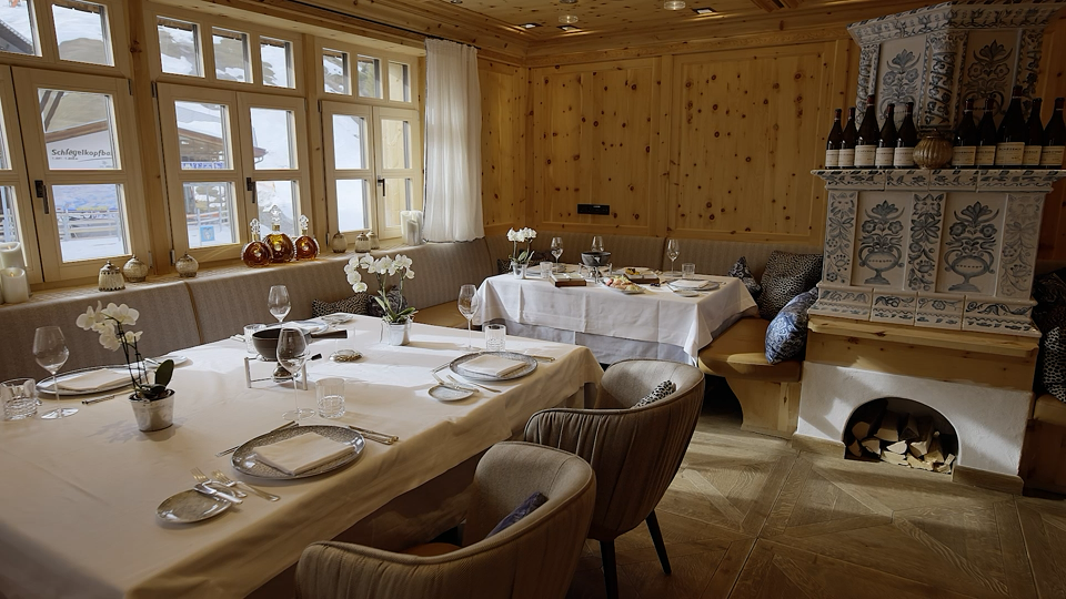 Gemütlicher Restaurantbereich mit gedeckten Tischen, Holzvertäfelung, frischen Blumen und traditionellem Kachelofen.